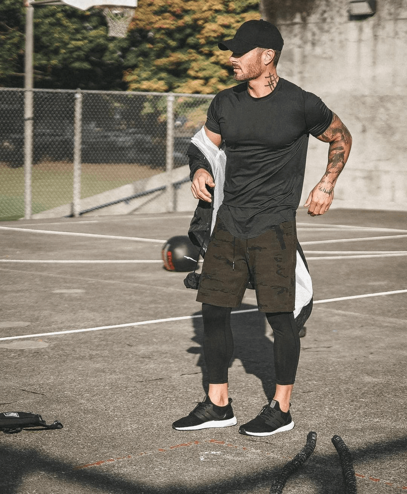 Man in black athletic gear standing on outdoor basketball court.