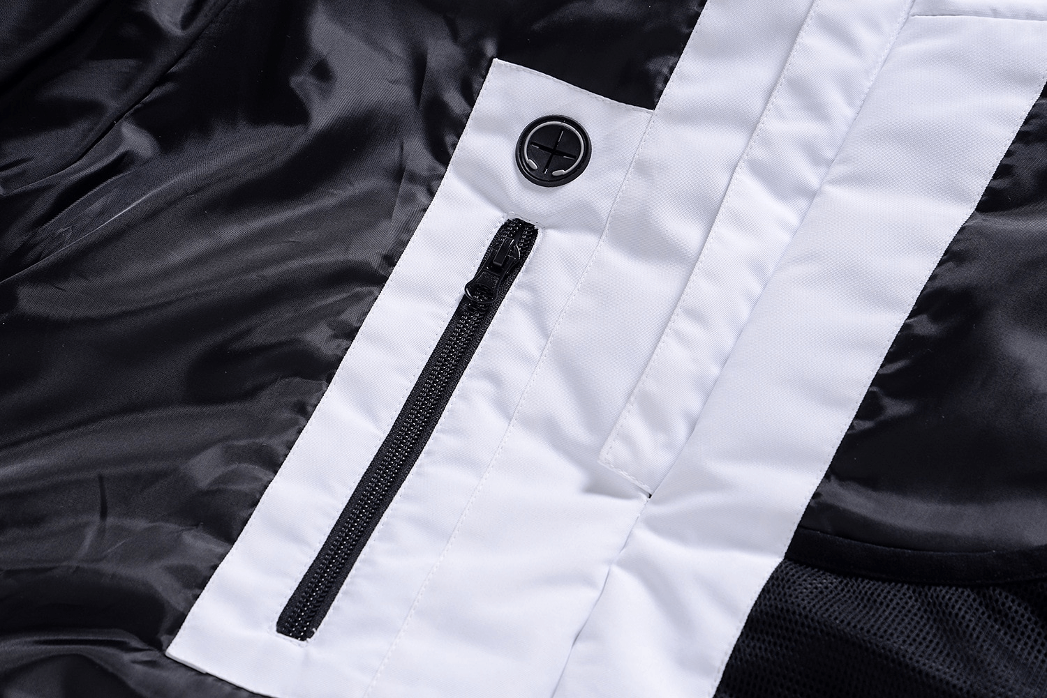 Close-up of black and white unisex ski jacket fabric showing a zippered pocket and button detail, perfect for snowboarding.