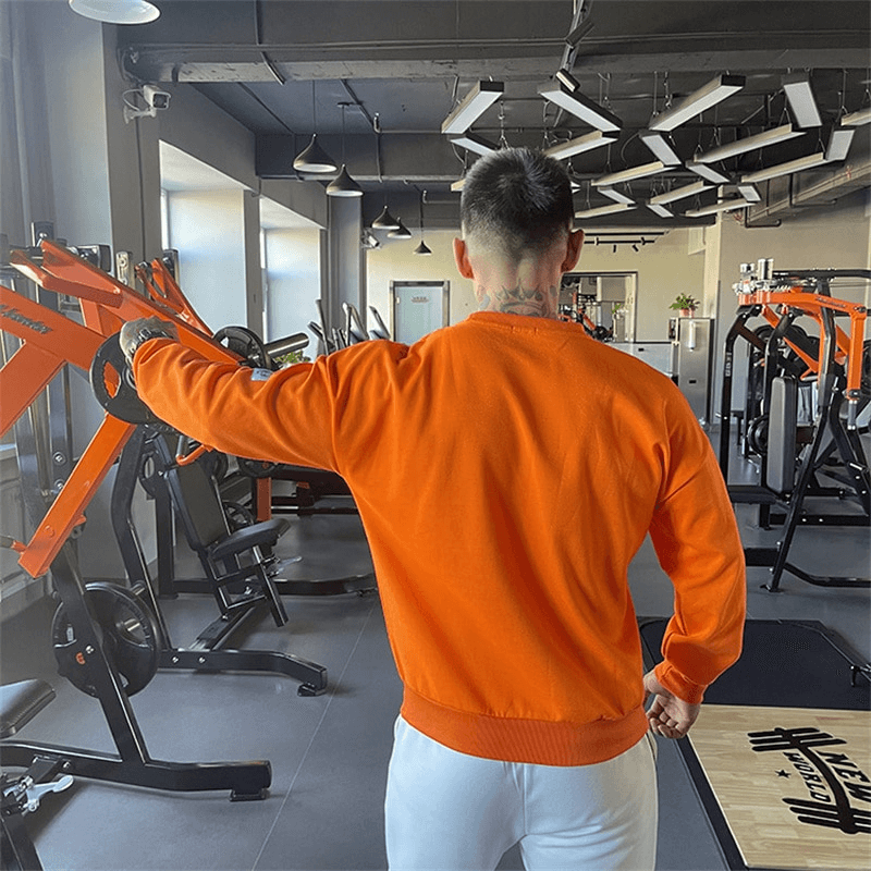 Man wearing orange loose men's sweatshirt in gym, showcasing O-neck collar and full-length sleeves.