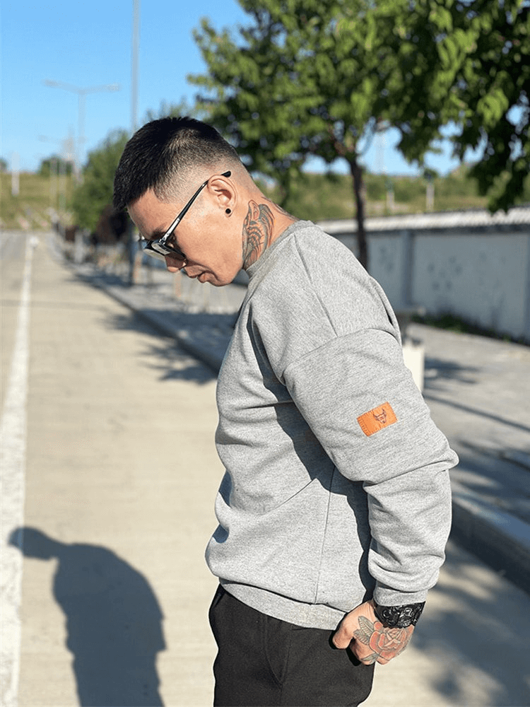 Stylish man wearing a gray loose-fitting sweatshirt with O-neck, enjoying a sunny day outdoors.