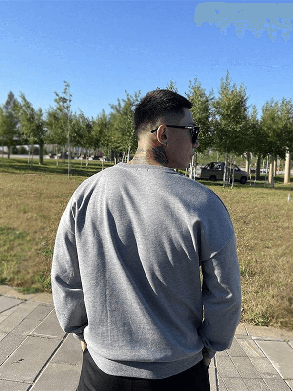 Man wearing loose grey sweatshirt outdoors, showcasing trendy fashion and comfort.