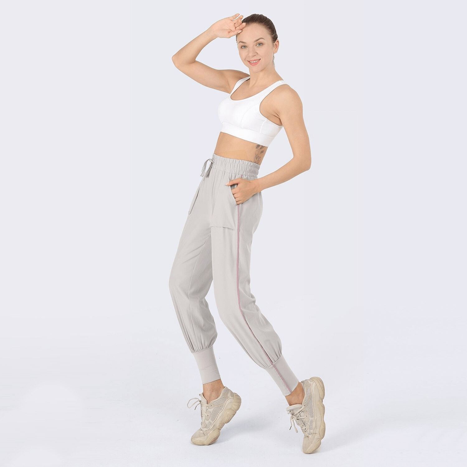 Smiling woman wearing grey drawstring waist sports jogging pants and white sports bra, posing in casual activewear.