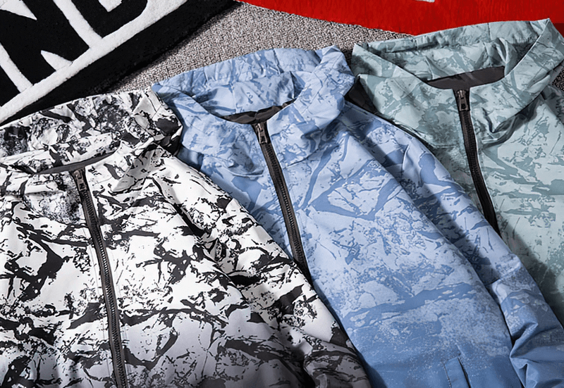 Colorful female zipper hooded jackets with artistic prints displayed on a soft background, showcasing lightweight windbreaker fashion.