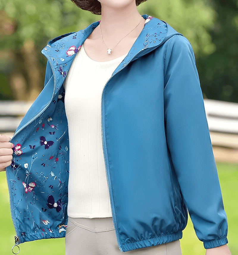 Woman wearing a blue reversible windbreaker with floral print and hood, showcasing the inside design.