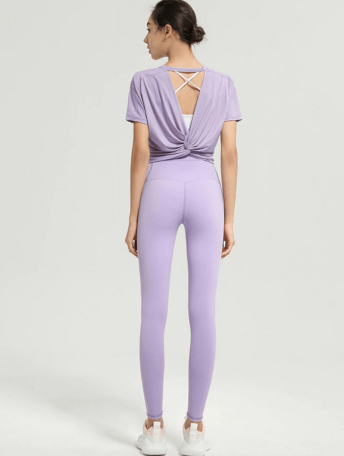 Woman wearing purple backless crop top and leggings set, showcasing sporty and stylish gym wear.