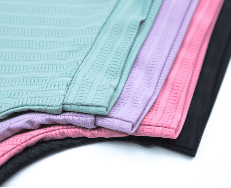 Colorful stack of ribbed gym crop tops in pastel green, purple, pink, and black made from stretchy polyester and spandex blend.