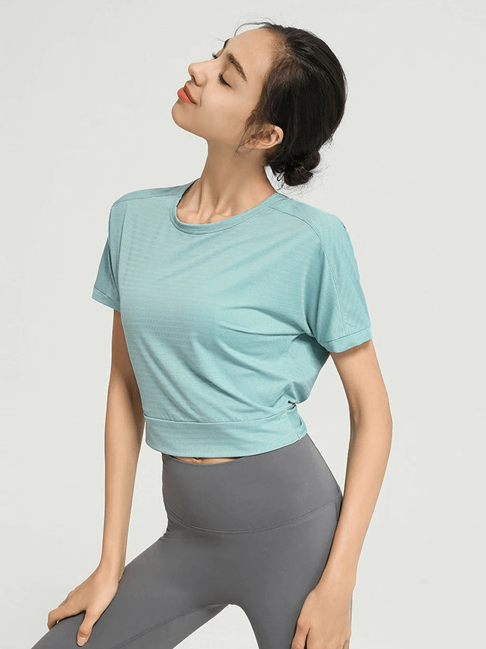 Woman wearing a teal loose backless fitness crop top with gray leggings, perfect for yoga and sports activities.