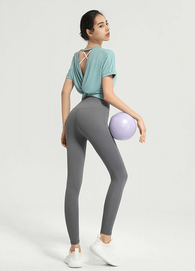 Woman in a backless fitness t-shirt holding a yoga ball, showcasing gym sportswear