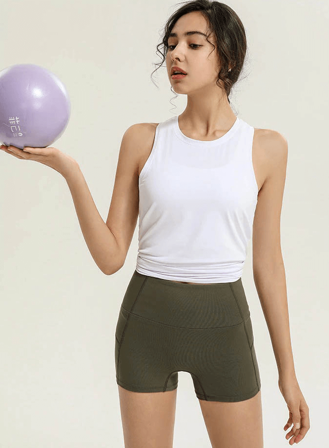 Woman wearing a white fitness tank top with a slit back holding a yoga ball, highlighting a breathable and stylish gym outfit.