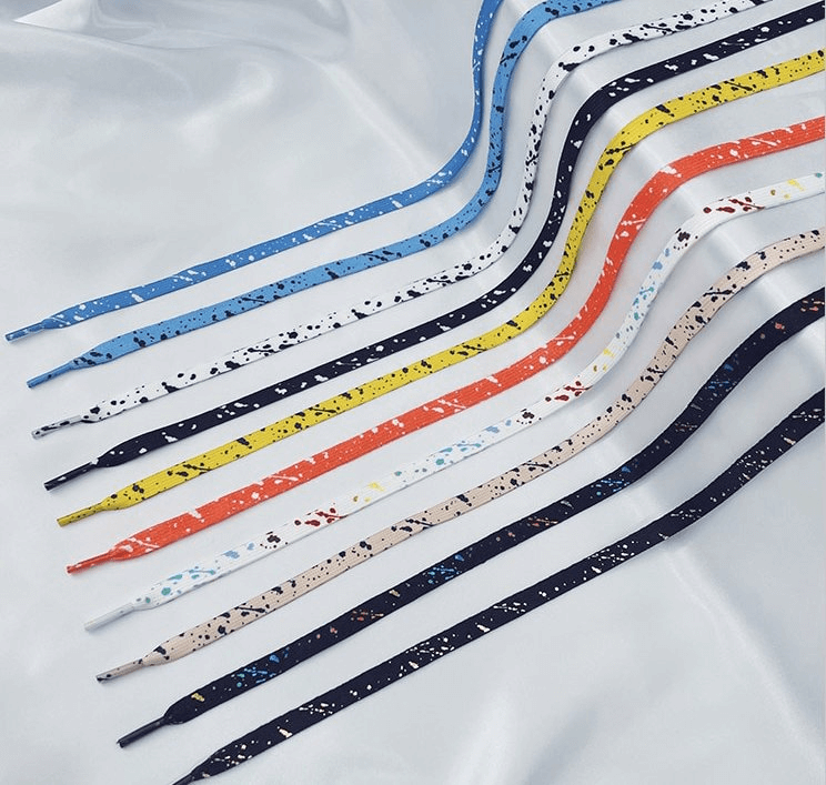Colorful flat shoelaces for sports shoes with speckled pattern displayed on a smooth surface.