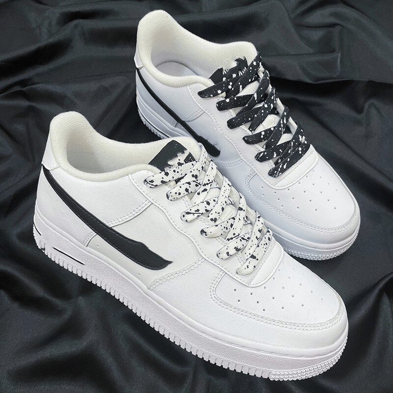 White sports shoes with black and white patterned shoelaces on a dark fabric background.