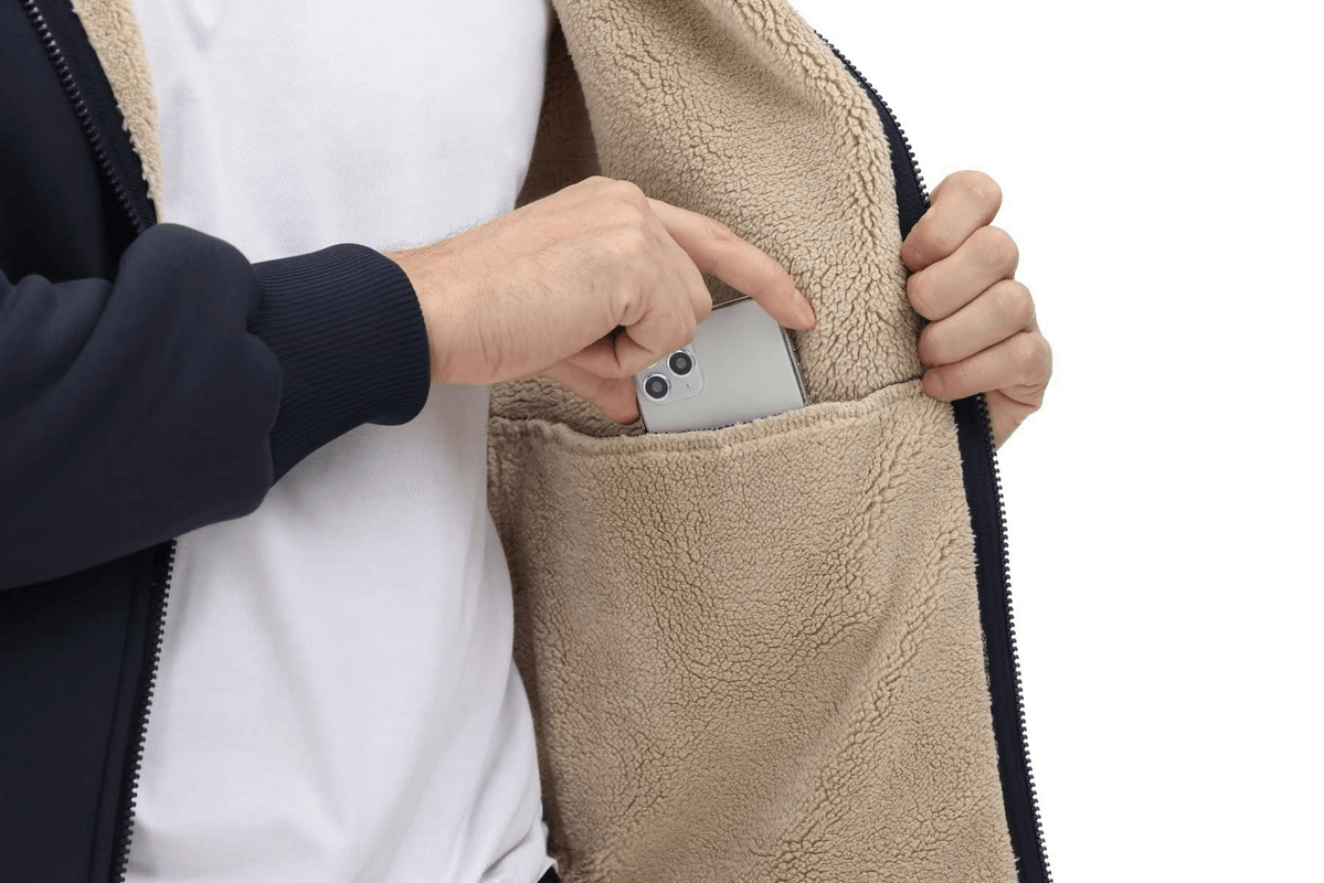 Person placing phone in pocket of fleece lining zipper sherpa jacket with hood, showcasing casual sportswear's practicality.