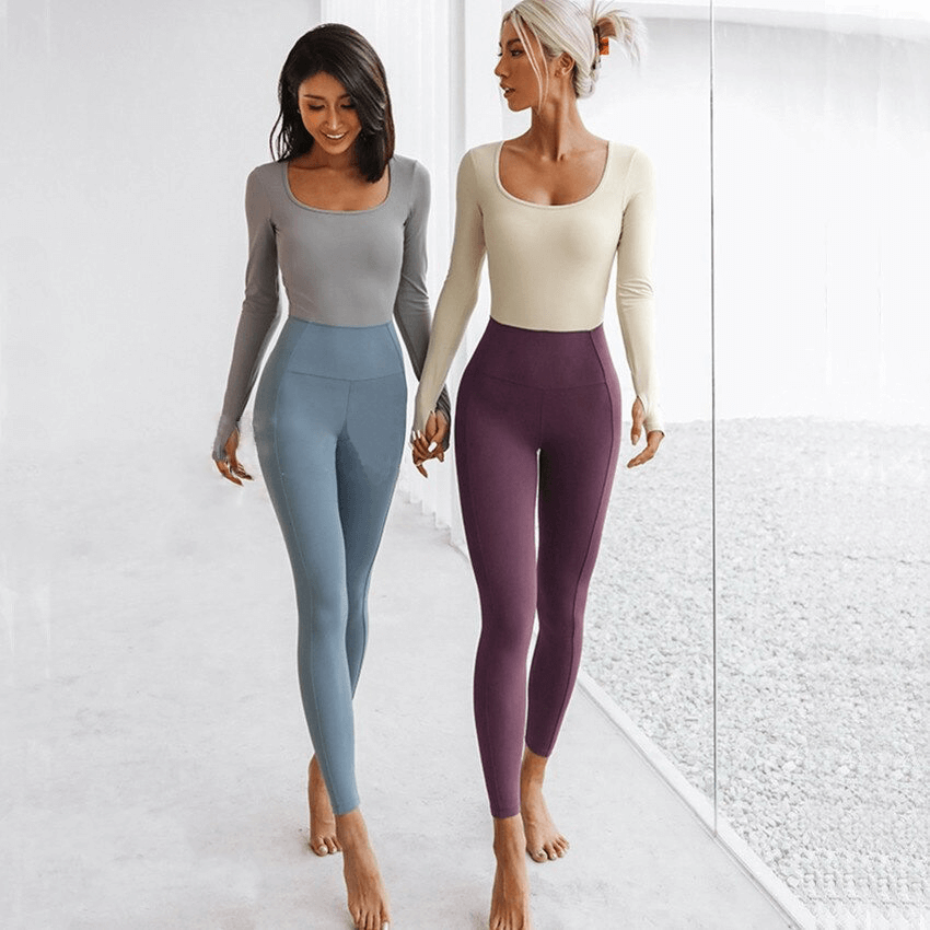 Two women in long-sleeve fitness jumpsuits walking in a bright room, showcasing stylish yoga apparel.