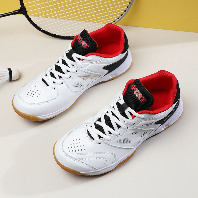 White lace-up flexible tennis shoes with red interior, featuring breathable material and rubber outsoles, set next to a badminton racket.