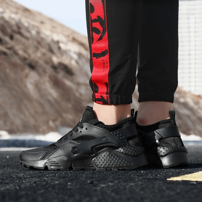 Person wearing black lace-up mesh running shoes on asphalt, highlighting their breathable and light sneaker design.