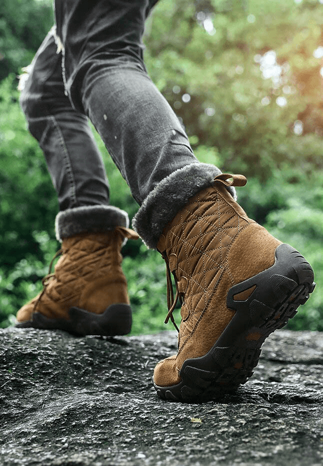 Person wearing lace-up waterproof non-slip mid-calf snow boots with fur, walking on rocky terrain.
