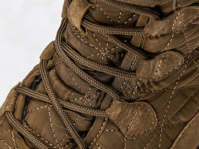 Close-up of lace-up waterproof snow boots with non-slip rubber soles, showcasing durable stitching and brown cotton fabric.