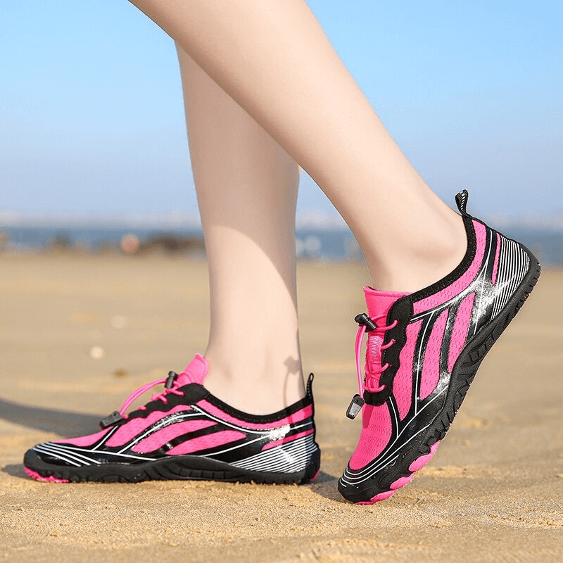 Person wearing pink breathable beach sneakers with elastic lacing on a sandy beach, showcasing superior traction outsole. Perfect for beach or pool.