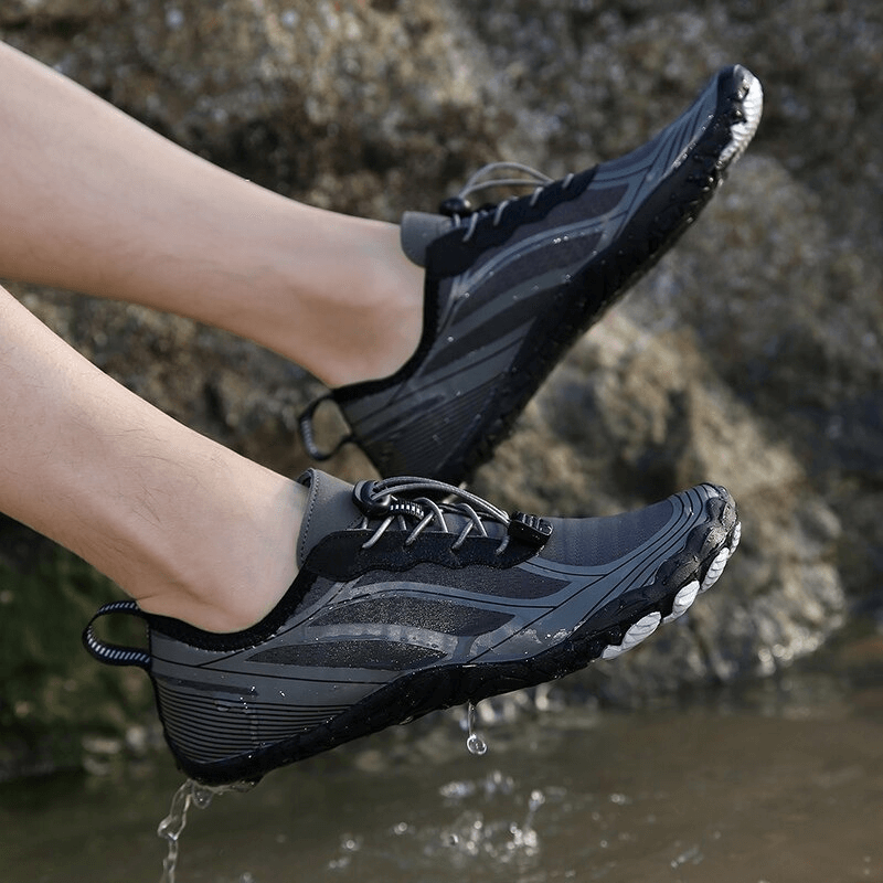 Person wearing light soft water shoes with elastic lacing, stepping in water near rocks. Ideal breathable beach sneakers, model SF0552.