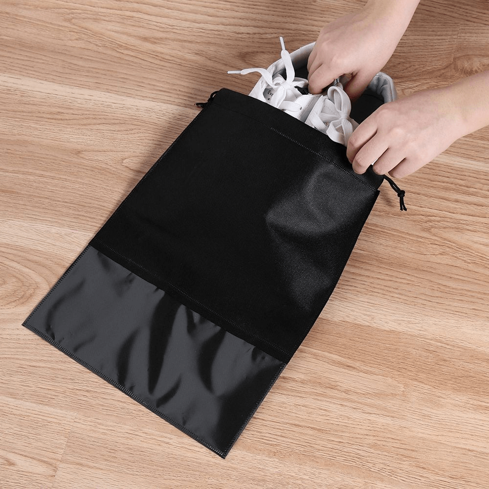 Hands placing sports shoes into a black lightweight quick-dry waterproof shoe bag made of non-woven fabric.