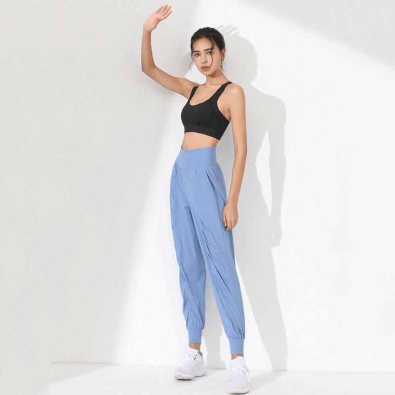 Woman wearing lightweight blue sports pants with wide belt and cuffs, ideal for yoga, featuring breathable polyester and spandex.