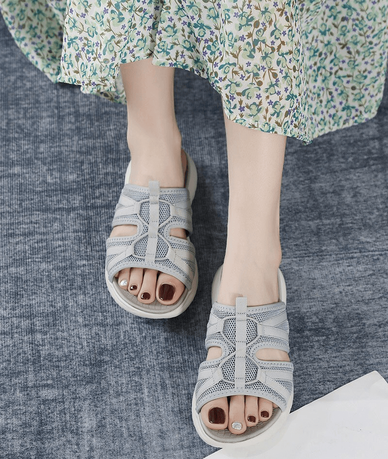 Woman wearing lightweight waterproof flat slippers with floral dress on blue carpet.