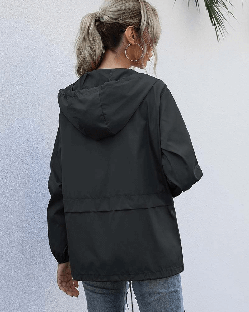 Back view of a woman wearing a lightweight waterproof black sport women's windbreaker jacket with hood, SF1168, against white wall.