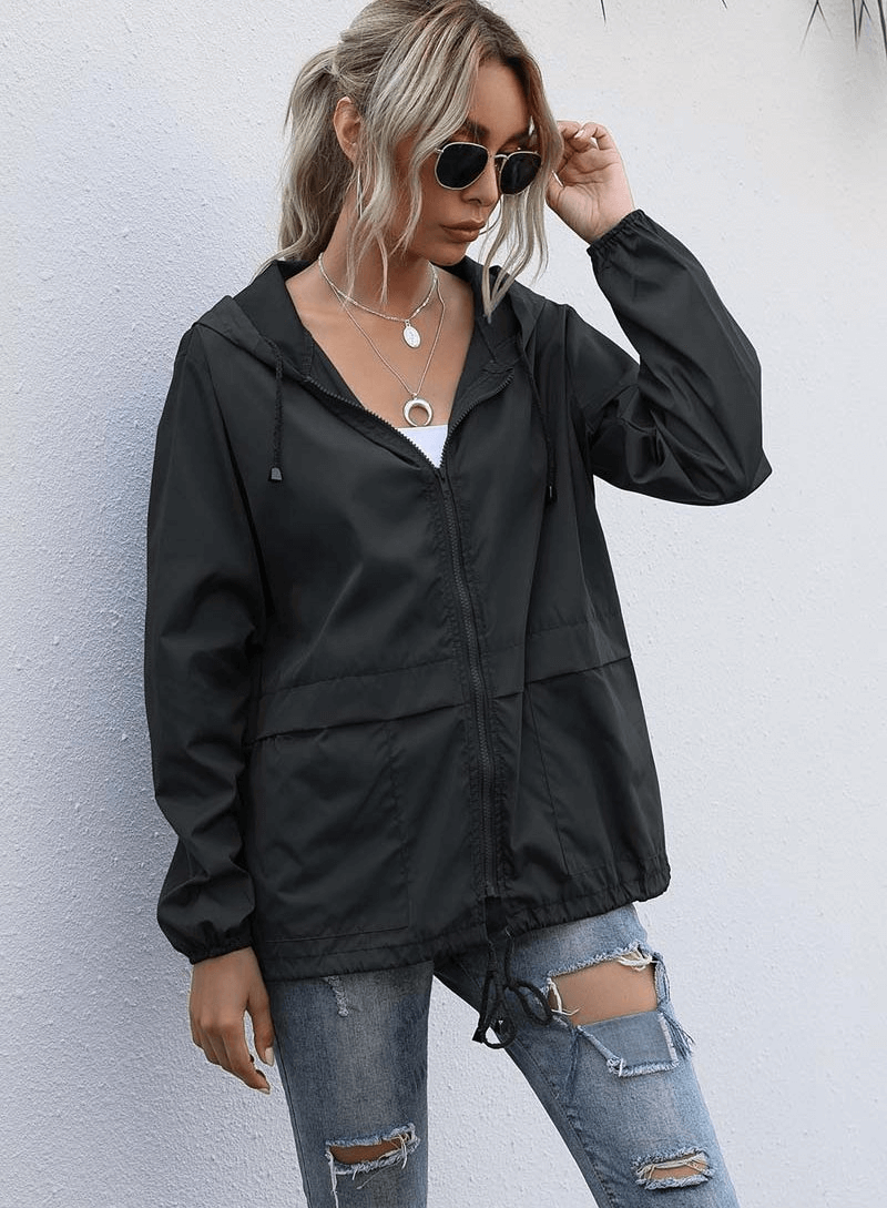 Woman wearing a lightweight waterproof sports jacket with hood, V-neck collar, and zipper closure, paired with ripped jeans, looking stylish.