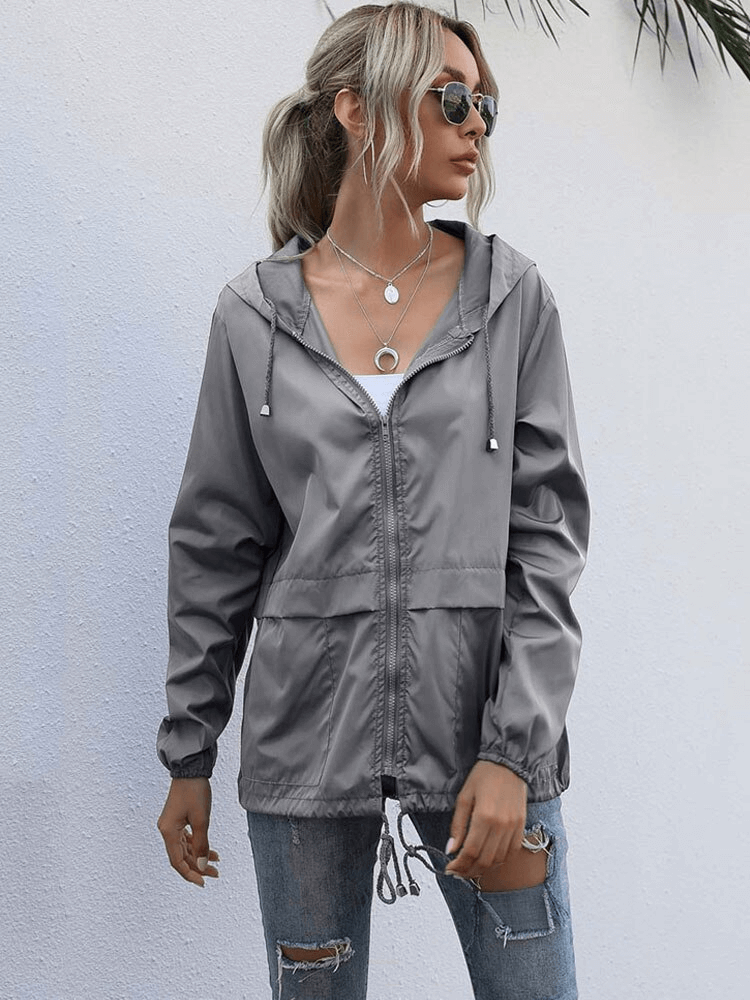 Woman wearing a grey lightweight waterproof sport jacket with hood, styled for a casual look.