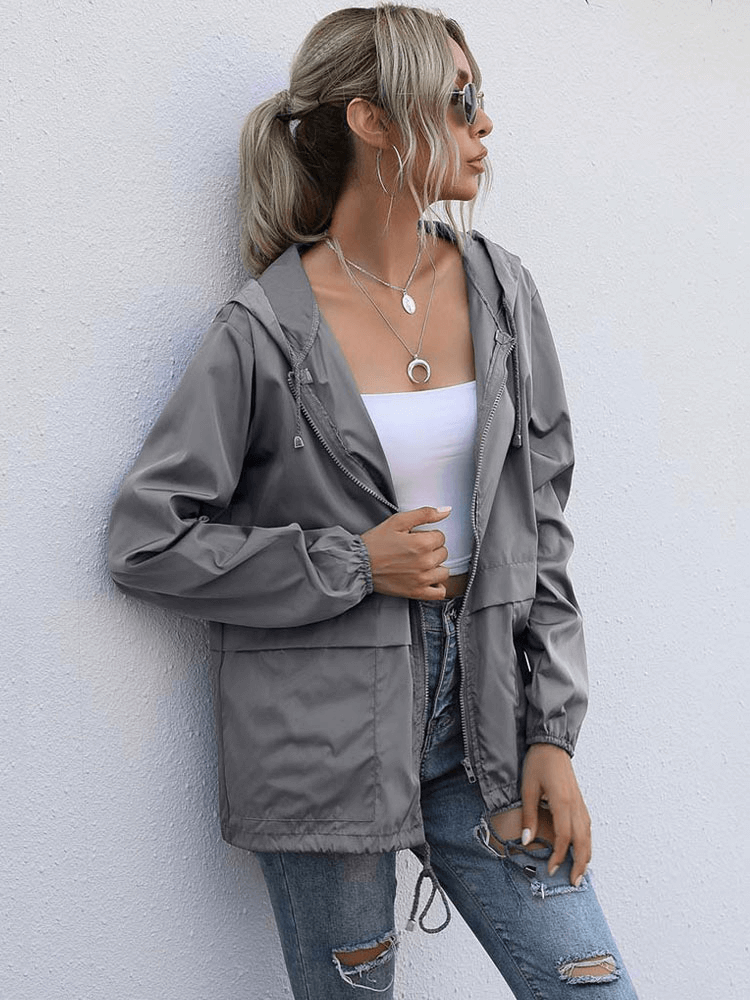 Woman wearing gray lightweight waterproof sport jacket windbreaker with hood, paired with white top and ripped jeans.