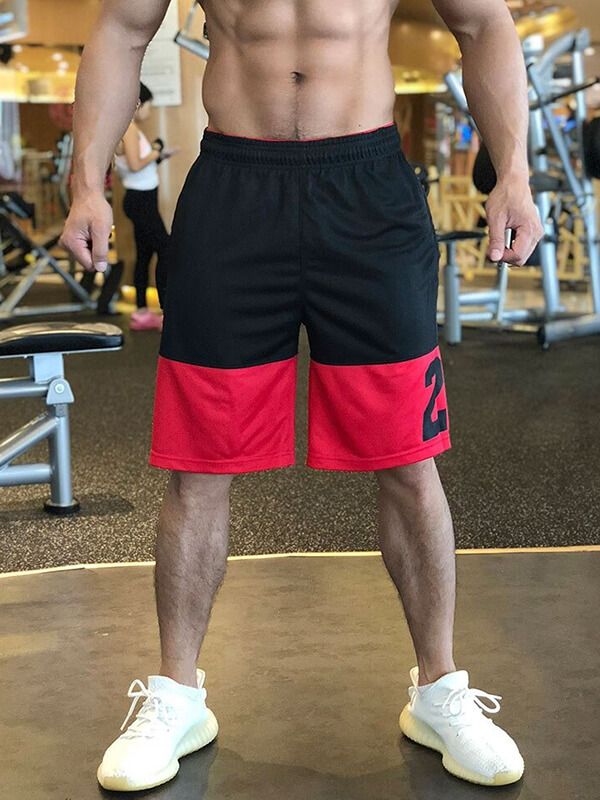 Man wearing loose basketball shorts with red accents, perfect for sports and gym workouts, featuring adjustable drawstring waistband.