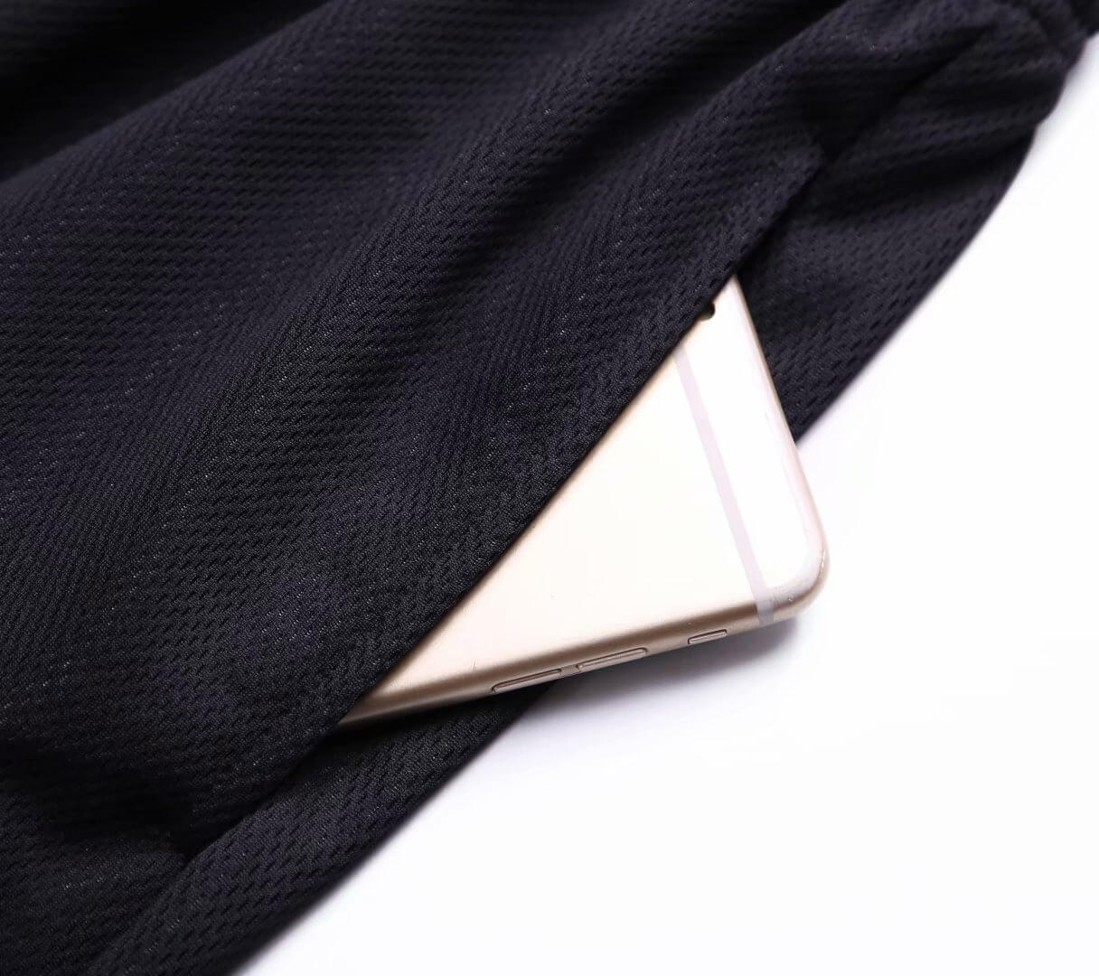 Close-up of a smartphone partially tucked into a pocket of black loose basketball shorts for men, made from polyester and spandex blend.