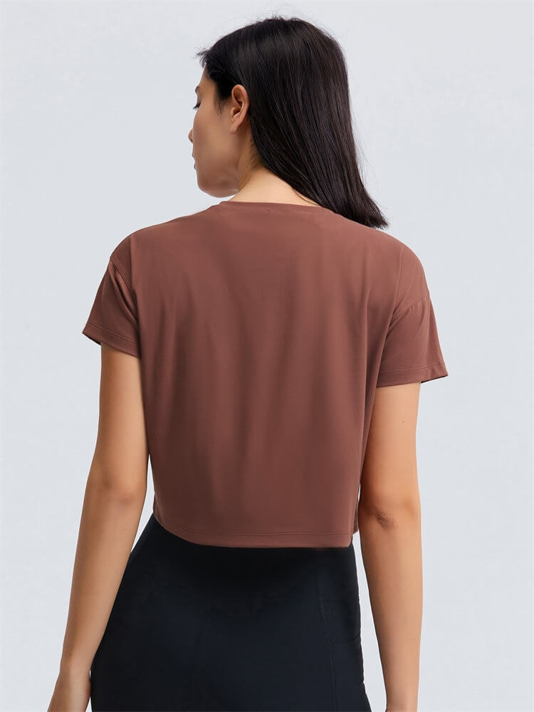 Back view of woman wearing a brown loose fit workout crop t-shirt for yoga, showing short sleeves and stretchy material.