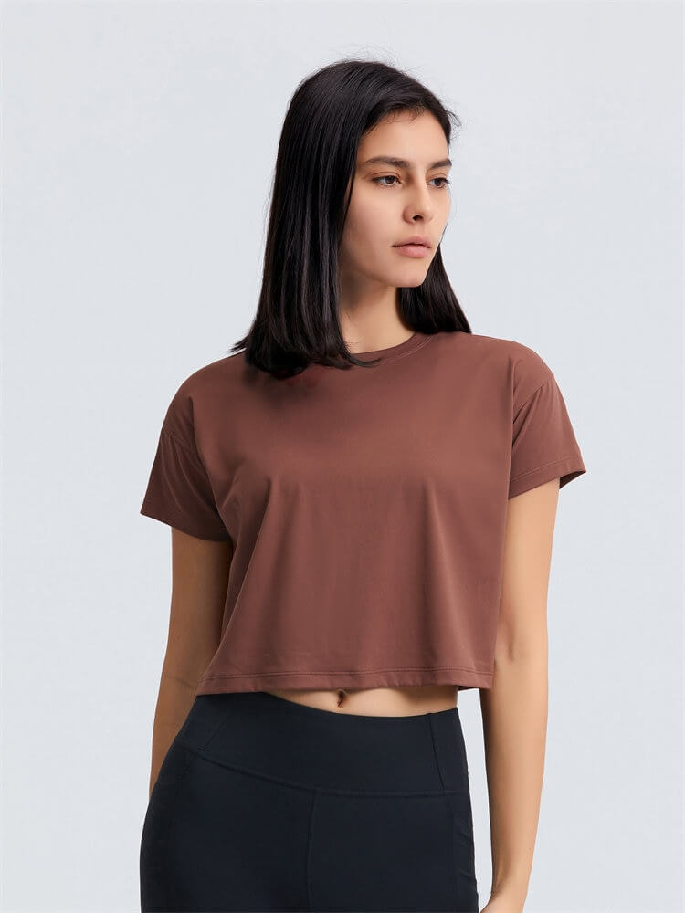 Woman wearing a brown loose fit workout crop t-shirt, ideal for yoga with short sleeves and comfortable fit, in a relaxed pose.