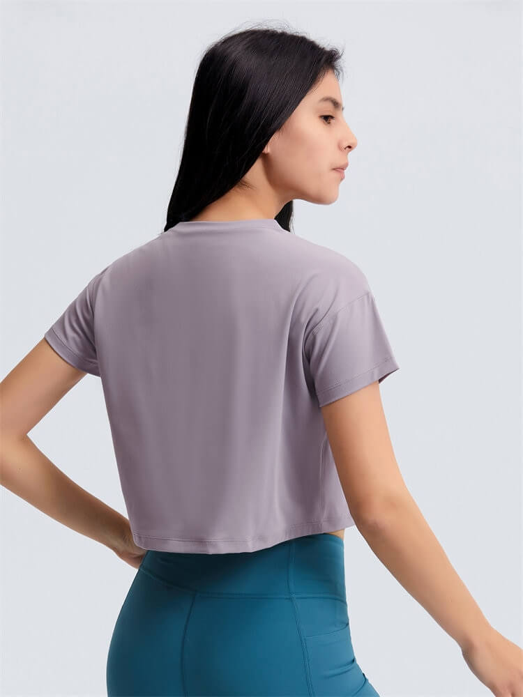 Woman wearing loose fit workout crop t-shirt for yoga, back view, showing short sleeves and comfortable fit. Stylish activewear.