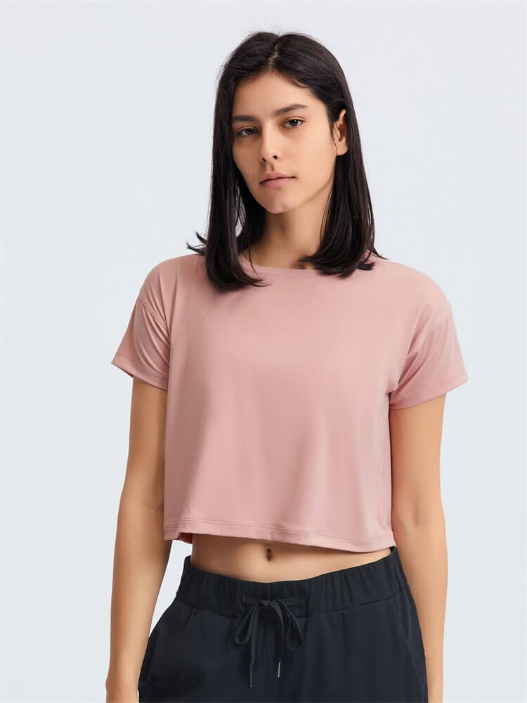 Woman wearing a pink loose fit cropped workout t-shirt, ideal for yoga, featuring short sleeves and a comfortable, breathable design.