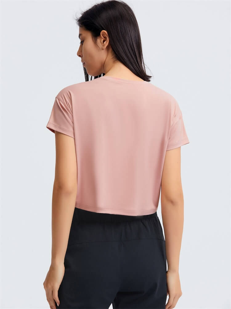 Woman wearing a loose fit workout crop t-shirt, perfect for yoga, in a soft pink hue, showcasing its breathability and flexibility.