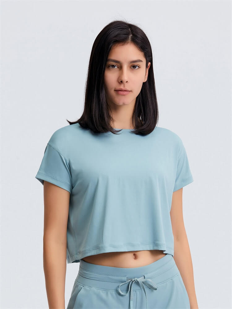 Woman modeling a Loose Fit Workout Solid Crop T-shirt, perfect for yoga, featuring a breathable nylon-spandex blend in a soft blue shade.