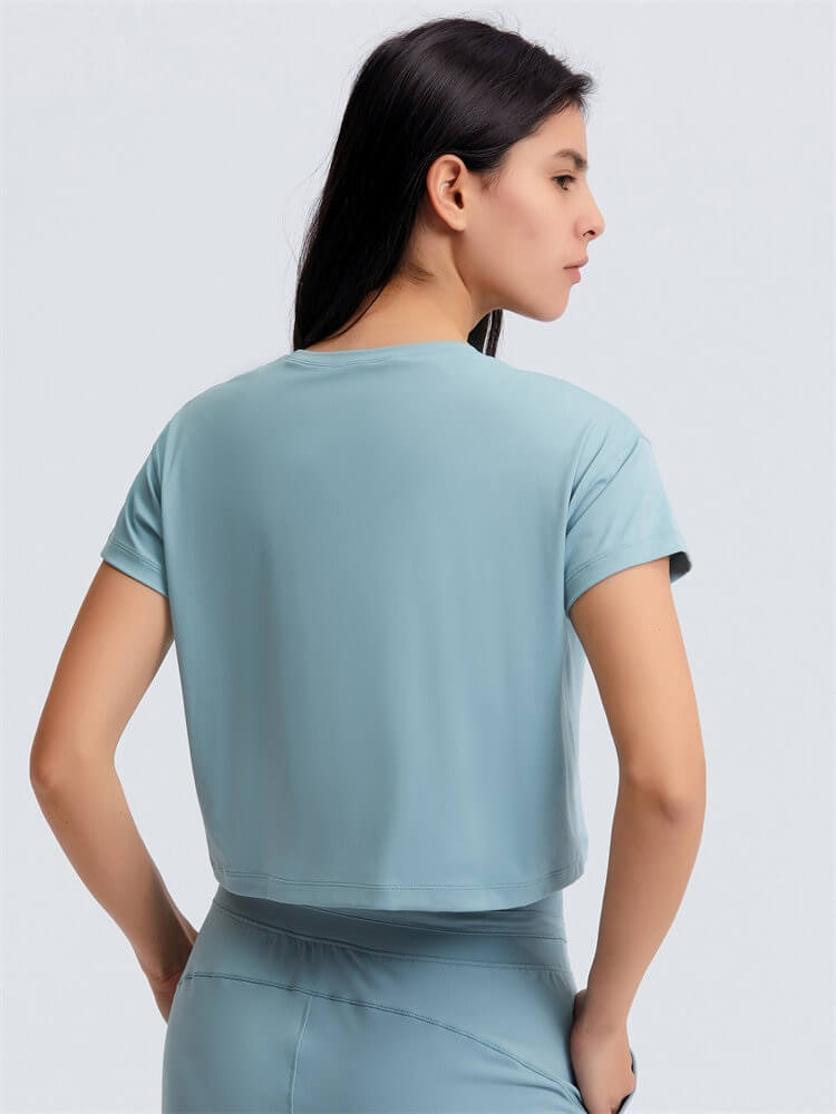 Back view of woman in loose fit solid crop t-shirt, perfect for yoga, showing breathable short sleeves and flexible nylon blend.