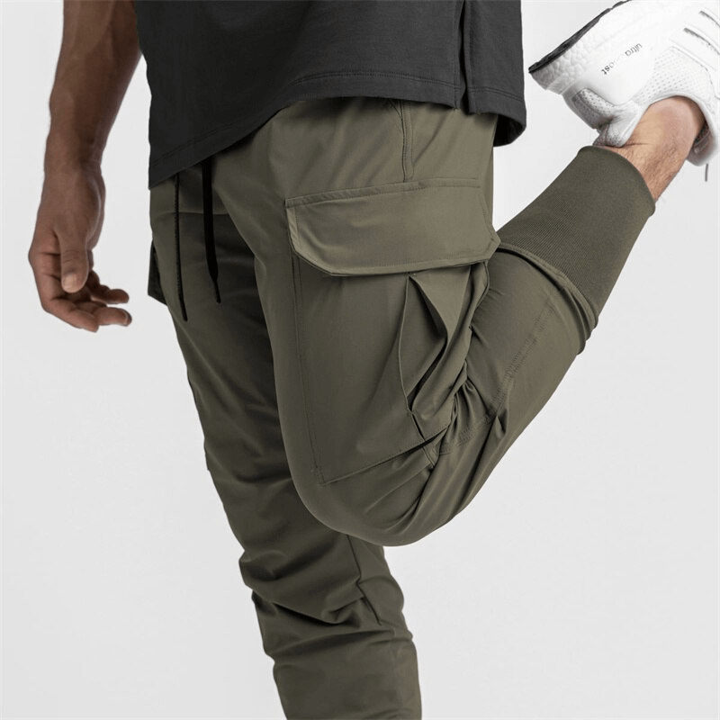 Man wearing loose slim elastic joggers with wide cuffs in khaki stretching leg during workout, styling casual sporty pants.