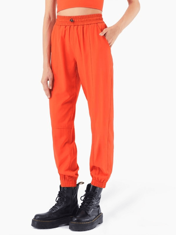 Model wearing loose women's high-waisted yoga pants in vibrant orange with black boots, showcasing style and comfort for yoga and leisure.