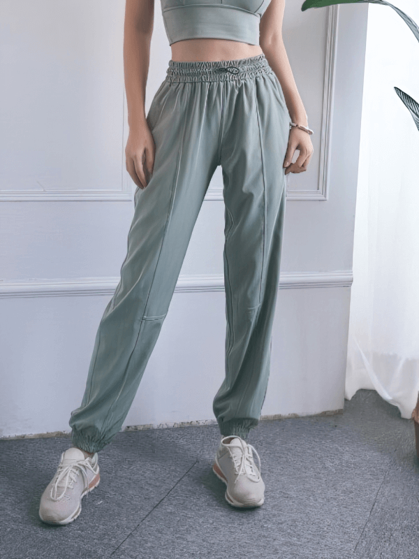 Woman wearing loose high-waisted yoga training pants in soft green, featuring a drawstring and comfortable fit for leisure activities.