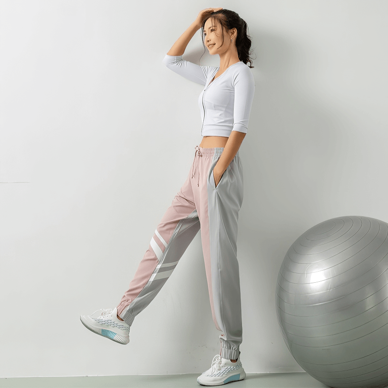 Woman wearing loose jogger pants with thin stripe, standing near exercise ball, showcasing comfort and style.