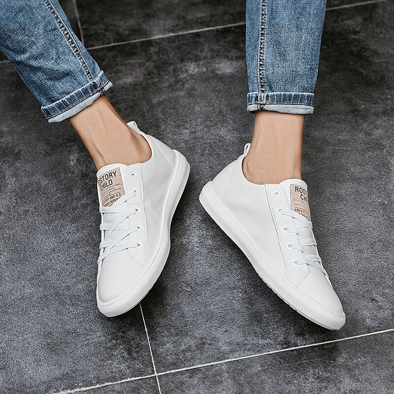 Stylish white leather casual shoes worn with rolled-up jeans on a tiled floor, perfect blend of fashion and comfort for men.