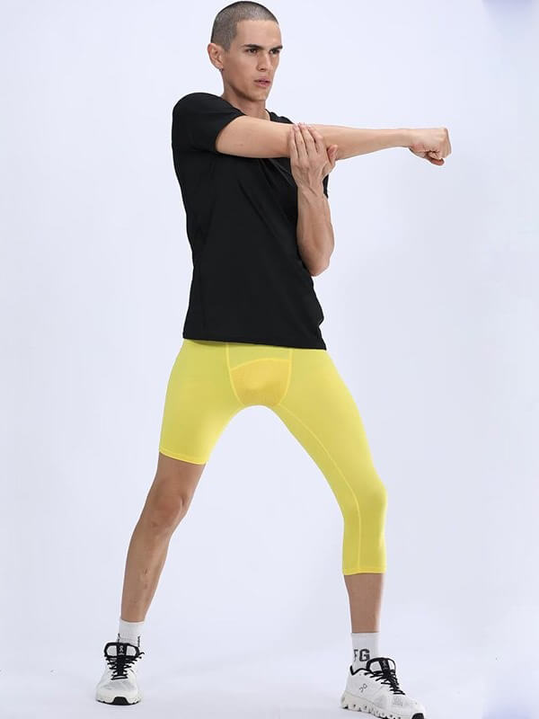 Man wearing yellow one-leg tights for sports, stretching arm; athletic gear for basketball or football, nylon-polyester blend.