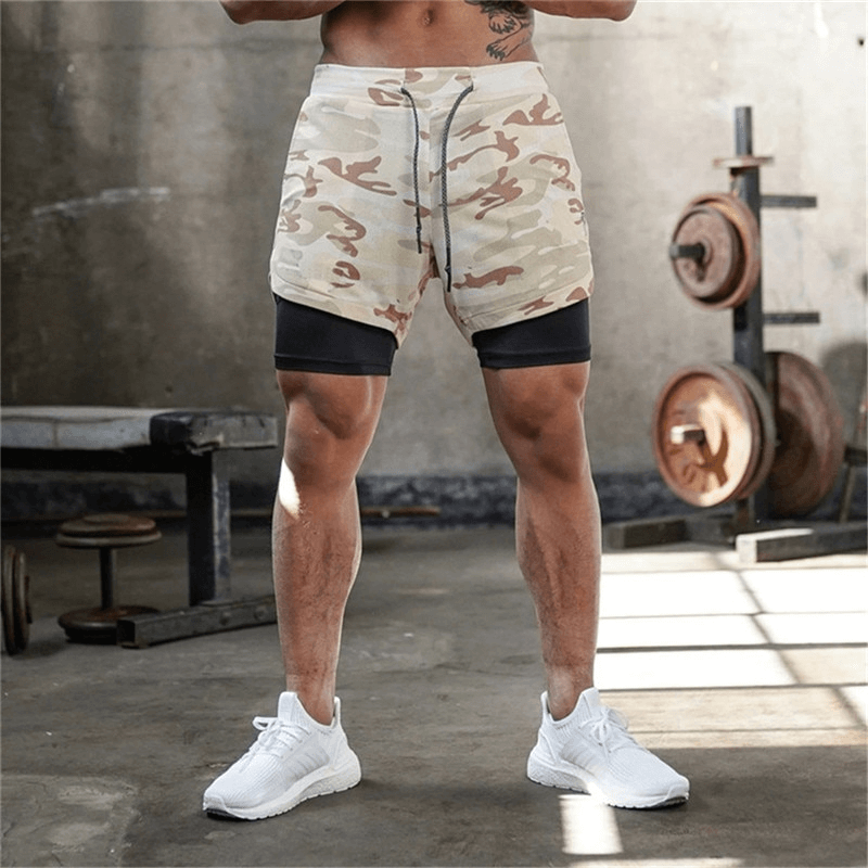 Man wearing male double-deck running shorts with camo print, standing in gym; quick dry, features pockets for convenient storage.