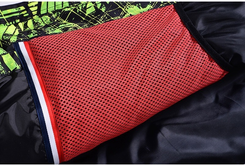 Close-up of red mesh pocket detail on men's ski jacket with black and green print, showcasing waterproof and windproof material.