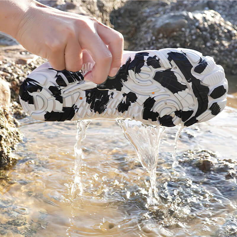 Hand squeezing draining water from breathable elastic water shoe for surfing, showcasing TPR outsole on rocky beach.