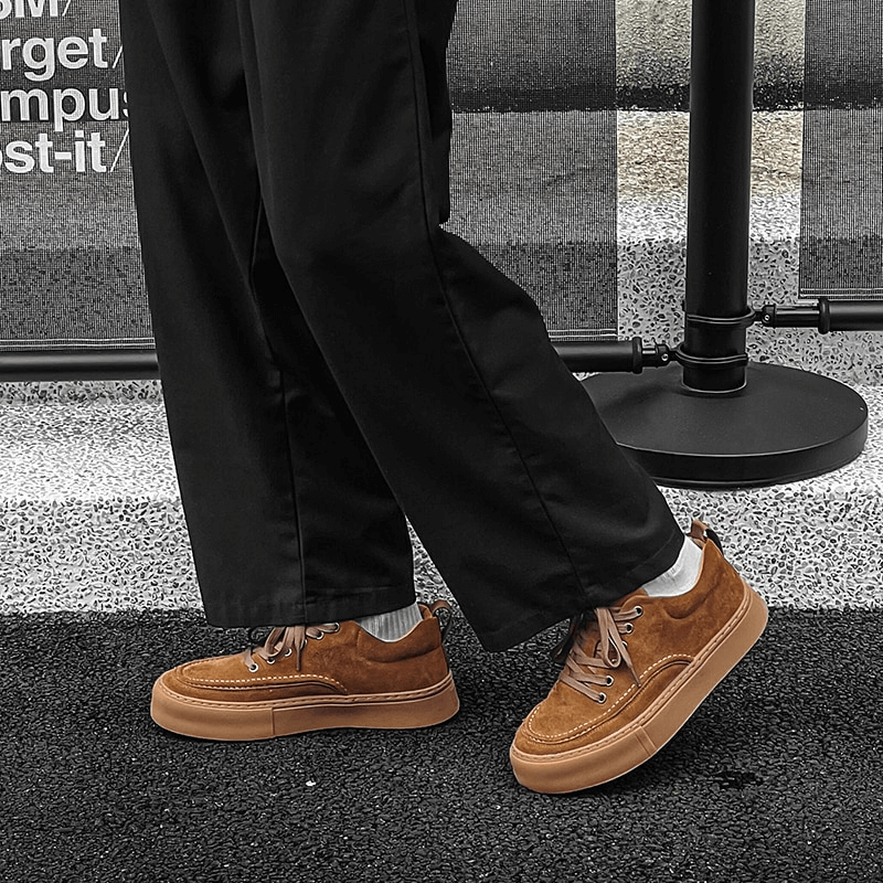 Person wearing brown leather stylish sneakers on a sidewalk, showcasing trendy and breathable casual footwear for men.