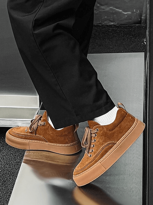 Men's breathable casual leather sneakers in brown with flexible rubber outsole, stylishly worn with black pants and white socks.